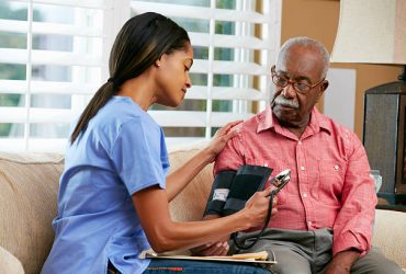 Nurse Visiting Senior Male Patient At Home Taking Blood Pressure